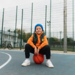 Adolescente sentado en una pelota en una pista de baloncesto