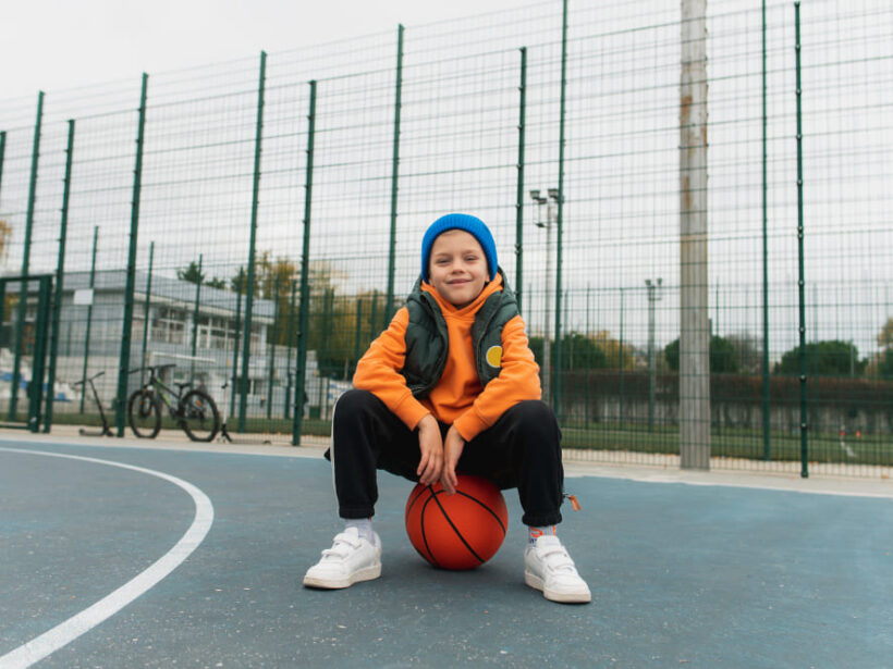 Adolescente sentado en una pelota en una pista de baloncesto