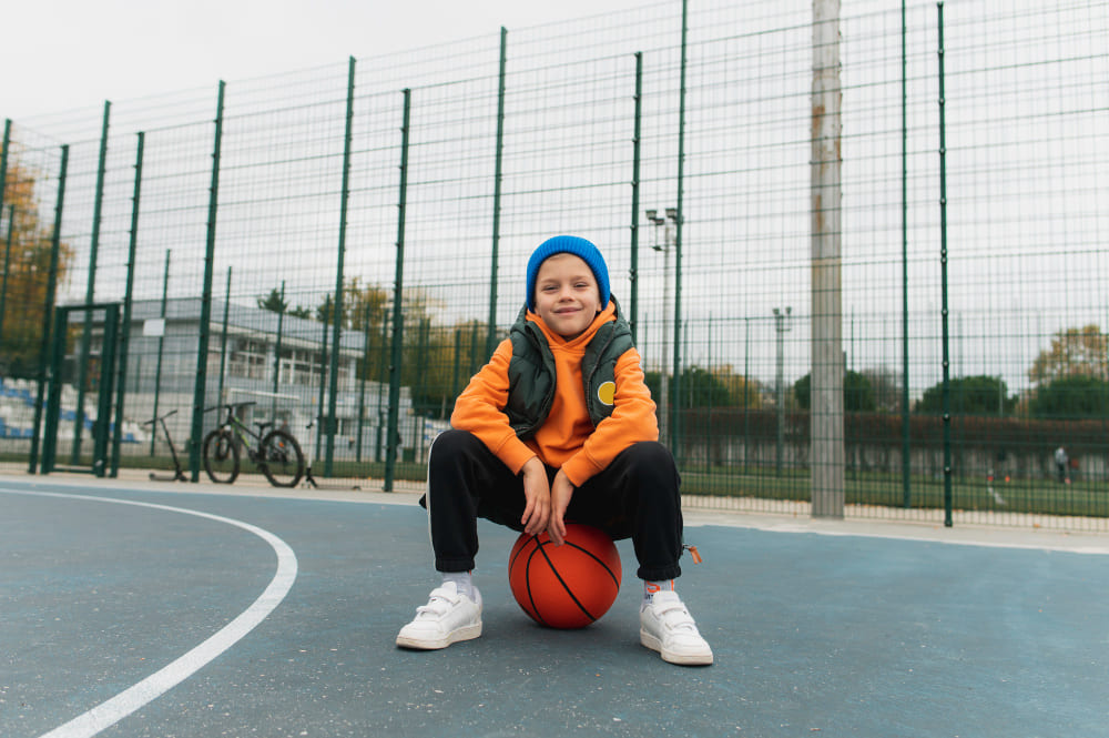 Adolescente sentado en una pelota en una pista de baloncesto